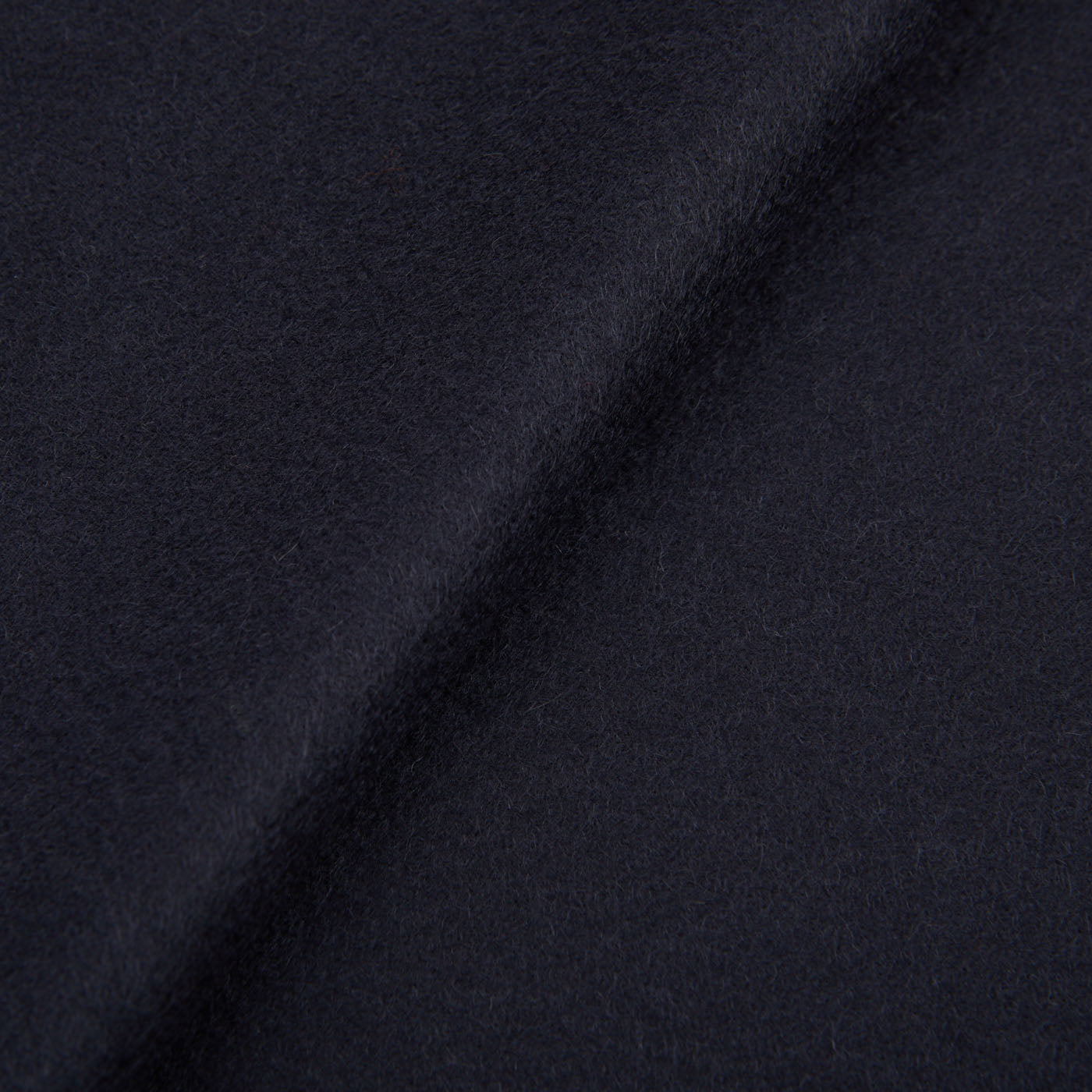 Close-up of a dark navy cashmere fabric with fringed endings, highlighting a diagonal seam. The texture appears soft and slightly fuzzy, embodying the luxurious feel of the Piacenza Cashmere Aeternum Scarf.