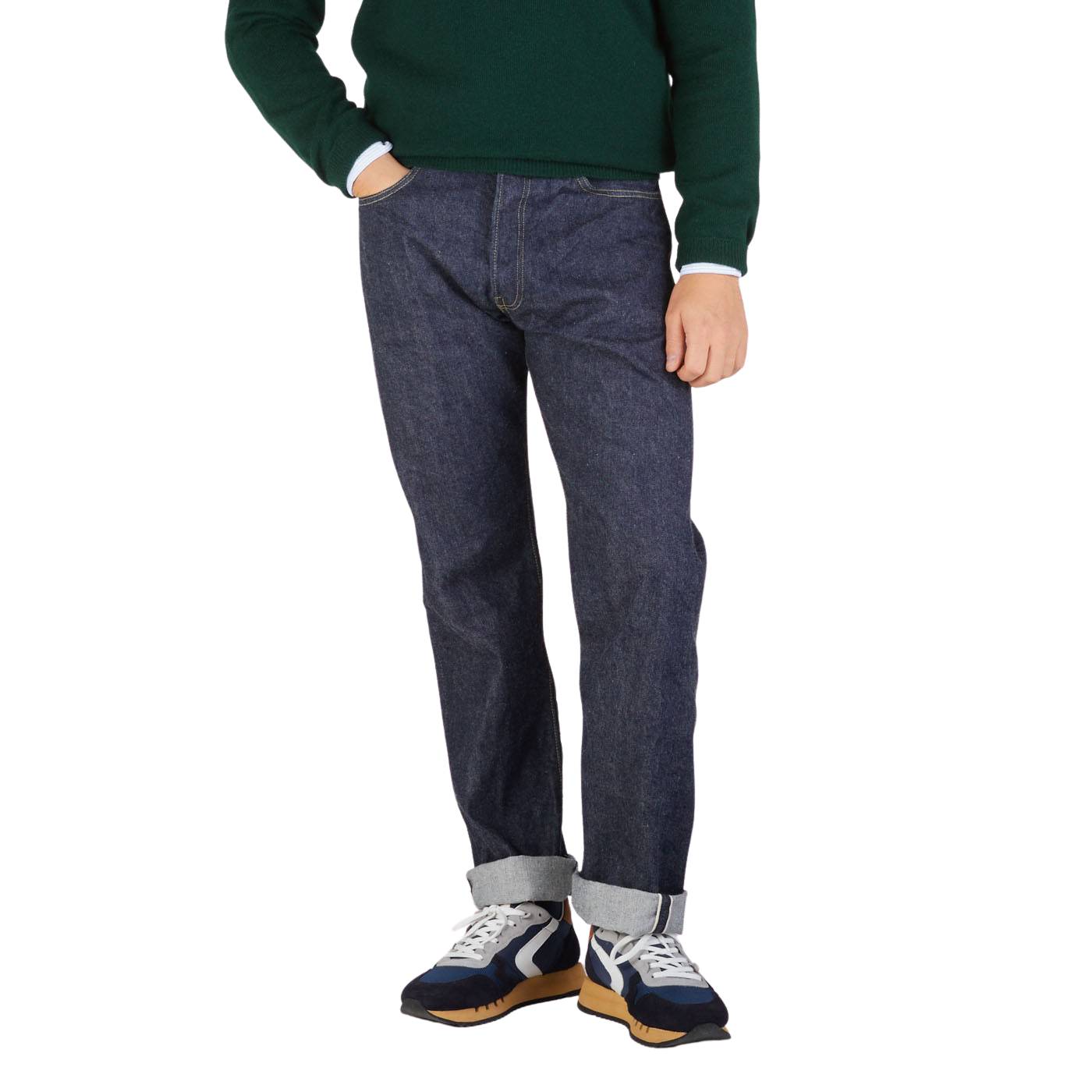 A person wearing Resolute dark blue selvedge denim jeans, a green sweater, and multicolored sneakers stands against a plain background, showing a side profile from waist to feet.