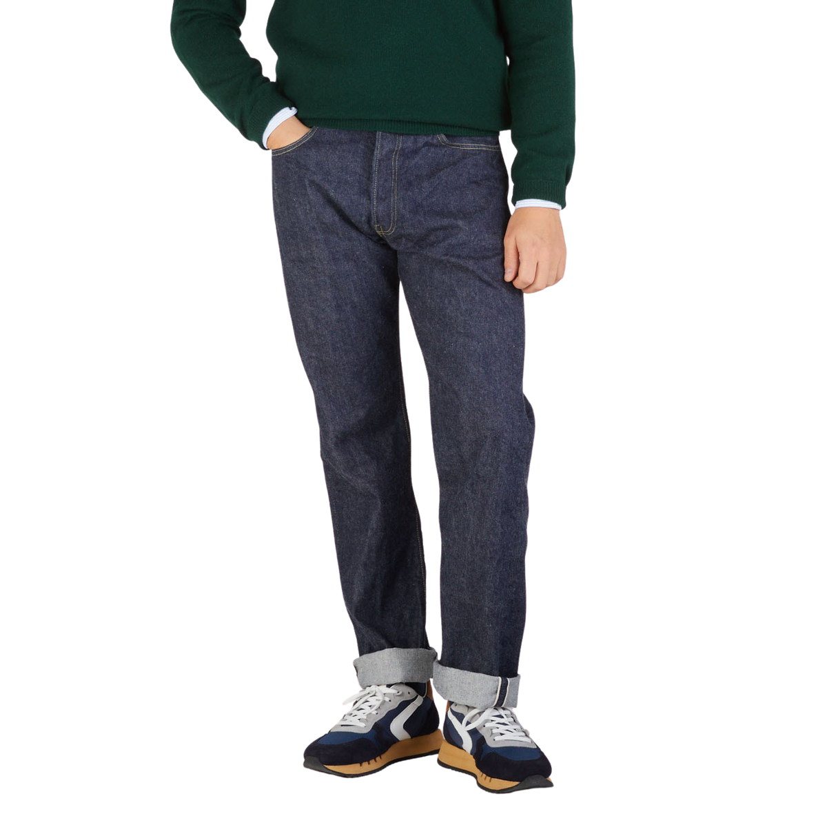 A person wearing Resolute dark blue selvedge denim jeans, a green sweater, and multicolored sneakers stands against a plain background, showing a side profile from waist to feet.