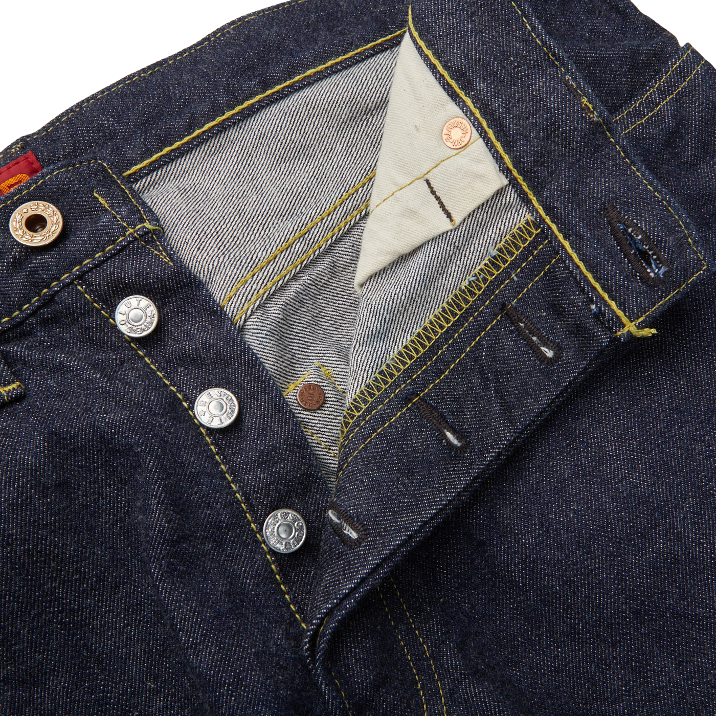 Close-up of a Resolute selvedge denim jacket with an open flap showing an inner striped lining and a mix of silver and brass buttons.