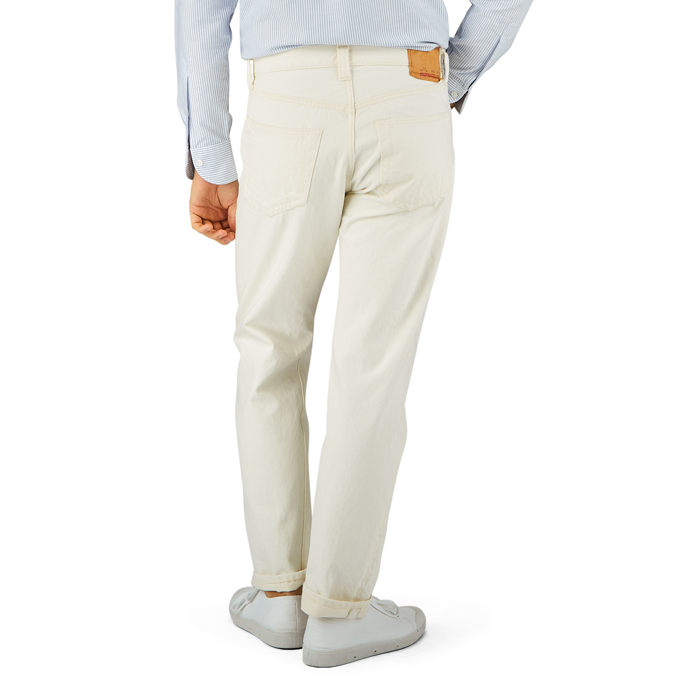 Man standing in a profile view wearing off-white Resolute Cream Cotton Selvedge 714 One Wash Jeans with a tucked-in light blue shirt and white sneakers.