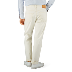 Man standing in a profile view wearing off-white Resolute Cream Cotton Selvedge 714 One Wash Jeans with a tucked-in light blue shirt and white sneakers.