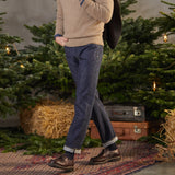 Man in a beige sweater and Resolute Dark Blue Cotton 714 One Wash Jeans walking across a rug with Christmas trees in the background.