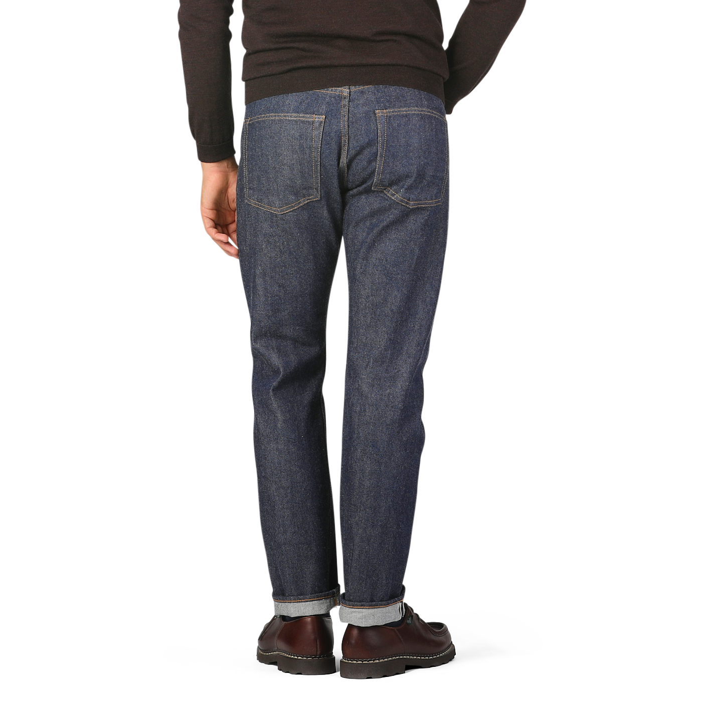 Person wearing Resolute Dark Blue Cotton 710 One Wash Jeans, a black sweater, and brown shoes, standing and facing away from the camera.