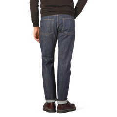 Person wearing Resolute Dark Blue Cotton 710 One Wash Jeans, a black sweater, and brown shoes, standing and facing away from the camera.