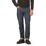 Person wearing a brown sweater with Dark Blue Cotton 710 One Wash Jeans by Resolute and brown shoes, standing against a plain background.