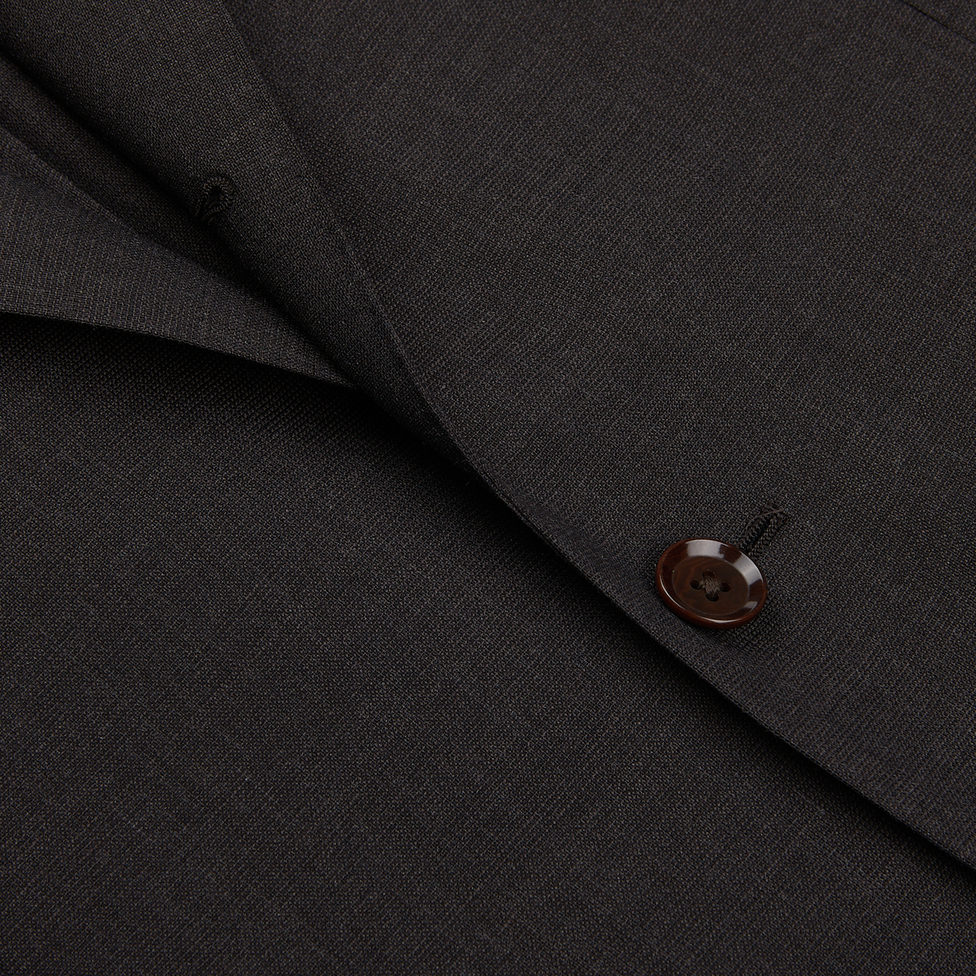 Close-up of a Ring Jacket Dark Brown High Twist Wool Suit fabric with a detailed view of a stitched button.