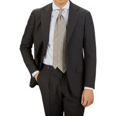 A man in a Ring Jacket dark brown high twist wool suit with a white shirt and plaid tie stands against a neutral background, cropped at the chest.