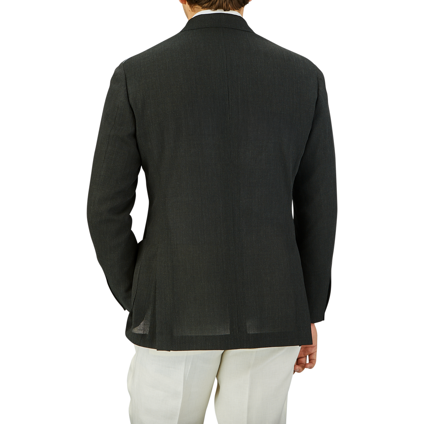 A man seen from behind, wearing a Ring Jacket dark green wool balloon travel blazer and white pants, standing against a plain grey background.