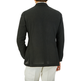 A man seen from behind, wearing a Ring Jacket dark green wool balloon travel blazer and white pants, standing against a plain grey background.