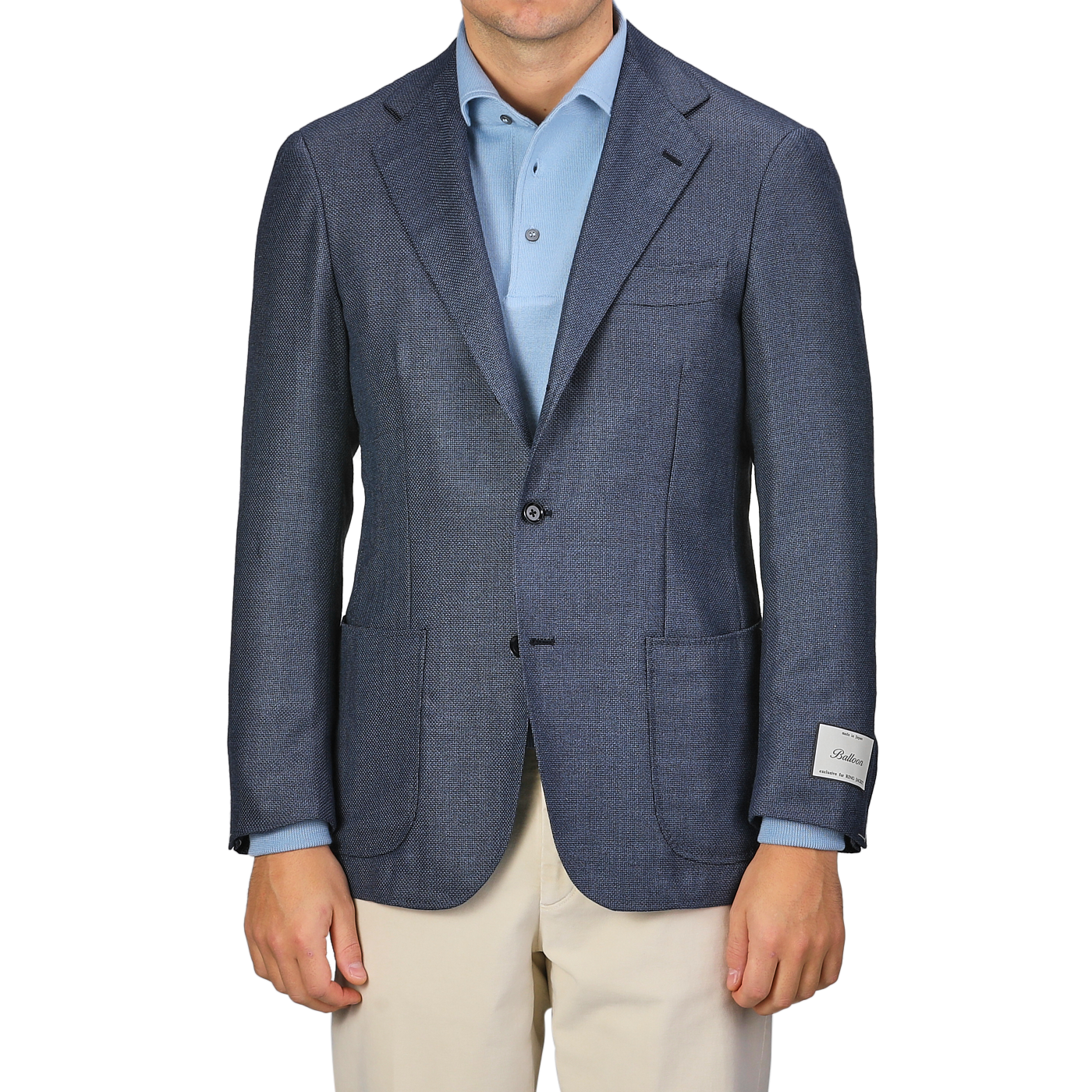 A person wearing the Ring Jacket Denim Blue Wool Balloon Travel Blazer over a light blue shirt and beige pants, with a visible tag on the sleeve, exuding an air of relaxed sophistication.