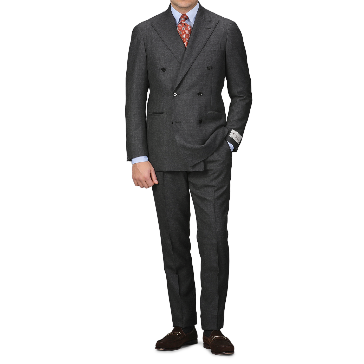 A person sporting the Ring Jacket Grey Calm Twist Wool DB Suit is elegantly poised against a white background. The suit, featuring a full canvas construction and crafted from fine wool fabric, is paired with a crisp white shirt, an orange patterned tie, and classic brown loafers.