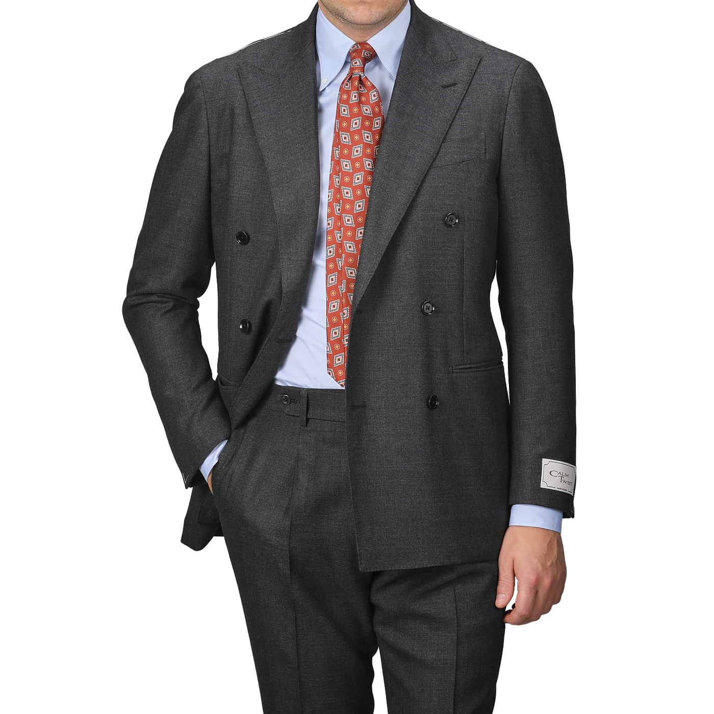 A person in a Grey Calm Twist Wool DB Suit by Ring Jacket, paired with a red patterned tie and hand in pocket, stands against a plain background.