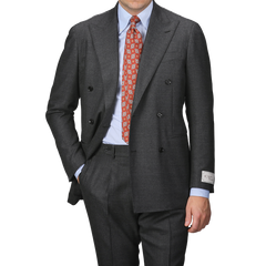 A person in a Grey Calm Twist Wool DB Suit by Ring Jacket, paired with a red patterned tie and hand in pocket, stands against a plain background.