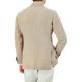 Rear view of a man in a Ring Jacket Light Beige Wool Balloon Travel Blazer and white pants standing against a gray background.