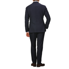 A person wearing the impeccably crafted Ring Jacket Navy Blue Calm Twist Wool Suit stands with their back to the camera, hands by their sides, against a plain background.