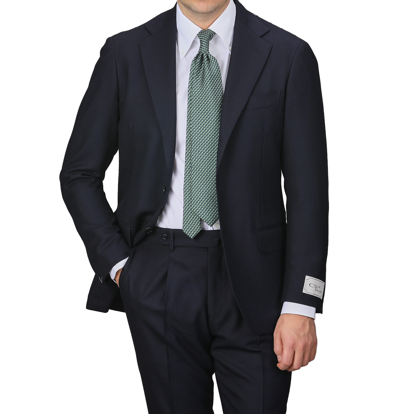 A man is standing against a plain background, wearing the Navy Blue Calm Twist Wool Suit by Ring Jacket, paired with a white shirt and a green tie, one hand casually tucked in his pocket.