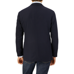 Rear view of a man wearing a Ring Jacket Navy Blue Wool Balloon Travel Blazer and jeans, standing against a light grey background.