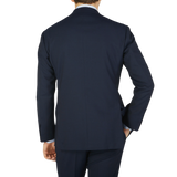 A man viewed from behind, wearing a navy blue high twist wool suit and matching pants in fresco fabric by Ring Jacket against a light background.
