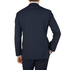 A man viewed from behind, wearing a navy blue high twist wool suit and matching pants in fresco fabric by Ring Jacket against a light background.