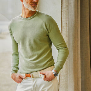 Man in an Aspesi sage green cotton piquet crew neck sweater with hand casually resting on a white belt.