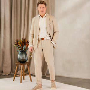 A man in a Sand Beige Washed Linen Unstructured Suit from Boglioli, possibly made of linen or Boglioli fabric, standing in front of a flower.