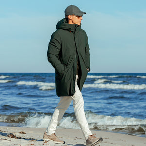 A man strolling on the beach in a Dark Green Padded Wilson Arctic Parka by Save The Duck.