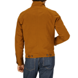 Man wearing a Sealup Tobacco Brown Cotton Harrington Waxed Jacket and blue jeans from a rear view.