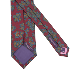 This Burgundy Paisley Printed Silk Tie by Seaward & Stearn is a handmade silk masterpiece. It features a red paisley design accentuated with blue and orange patterns, complemented by a luxurious purple lining and a discreet logo on the inner side.