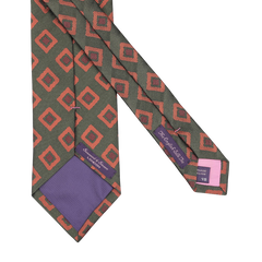 A Seaward & Stearn handmade silk tie, named the Green Orange Geometric Silk Tie, with a red geometric pattern on a dark background, featuring purple labels and a charming purple tip.