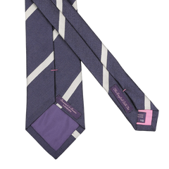 A navy blue silk tie with cream diagonal stripes, subtly showing pink labels inside, expertly handmade in England by Seaward & Stearn.