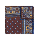 A neatly folded, square-shaped Chocolate Recioto Silk Pocket Square from Sera Fine Silk showcases a vibrant paisley pattern in blue, brown, and yellow tones with one corner visible. This luxury silk pocket square is made in Italy.