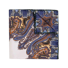 The Cortina Blue Silk Pocket Square by Sera Fine Silk is a folded silk accessory featuring an intricate paisley pattern in blue, orange, and brown colors on a white background. It boasts elegant hand-rolled edges.