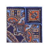 The Licorice Barolo Silk Pocket Square by Sera Fine Silk features an elaborate folded design with a navy blue paisley pattern, accented by orange and light blue hues. Crafted from pure Como silk, it boasts hand-rolled edges.