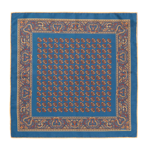 Introducing the Nutmeg Montepulciano Silk Pocket Square by Sera Fine Silk—a luxurious accessory featuring a distinctive blue pattern with a repeated central design and an intricate border adorned with ornamental motifs. Perfect for the season, this silk pocket square boasts elegant hand-rolled edges.