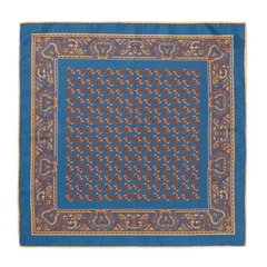 Introducing the Nutmeg Montepulciano Silk Pocket Square by Sera Fine Silk—a luxurious accessory featuring a distinctive blue pattern with a repeated central design and an intricate border adorned with ornamental motifs. Perfect for the season, this silk pocket square boasts elegant hand-rolled edges.