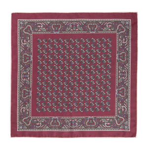 A luxurious pocket square named the Rose Montepulciano by Sera Fine Silk, crafted from exquisite Como silk, featuring an intricate paisley pattern with a detailed border and repeating smaller designs in the center. The edges are meticulously hand-rolled to complete this maroon masterpiece.