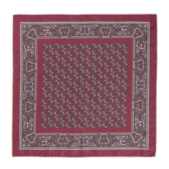 A luxurious pocket square named the Rose Montepulciano by Sera Fine Silk, crafted from exquisite Como silk, featuring an intricate paisley pattern with a detailed border and repeating smaller designs in the center. The edges are meticulously hand-rolled to complete this maroon masterpiece.