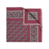 The Rose Montepulciano Silk Pocket Square by Sera Fine Silk is a folded maroon accessory with an intricate paisley pattern in blue, white, and light brown hues, featuring elegant hand-rolled edges.