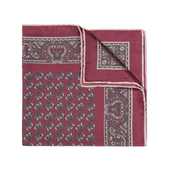 The Rose Montepulciano Silk Pocket Square by Sera Fine Silk is a folded maroon accessory with an intricate paisley pattern in blue, white, and light brown hues, featuring elegant hand-rolled edges.