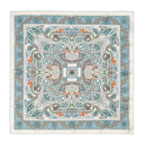 The Vernazza Cream Silk Pocket Square by Sera Fine Silk is a luxurious square piece of fabric adorned with an intricate pattern featuring blue, green, and orange paisley designs on a white background. Made from Como silk, this pocket square features hand-rolled edges for a refined finish.