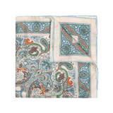 The Vernazza Cream Silk Pocket Square by Sera Fine Silk is expertly folded and showcases an intricate paisley design in shades of blue, green, and orange on an ivory background, complete with hand-rolled edges.