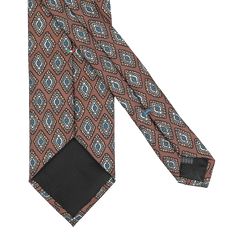 A tie from Stefano Cau featuring a luxurious Italian Como silk with a cinnamon brown base and a repeating geometric diamond pattern in blue, white, and black, laid flat.