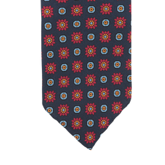 A detailed view of the Stefano Cau Dark Blue Flower Printed Silk Unlined Tie, made from luxurious Italian Como silk, is set against a blue background and features a pattern of red and orange flowers within squares.