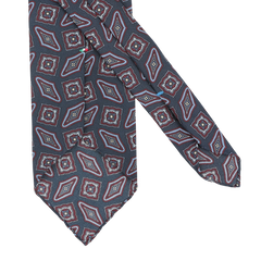 A dark blue kilim-printed silk unlined tie from Stefano Cau showcases a geometric red, blue, and white design, reflecting the elegance of Italian craftsmanship.