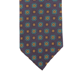 Close-up of a Stefano Cau tie meticulously crafted from luxurious Italian Como silk, showcasing a pattern of purple flowers with yellow squares against a dark background.