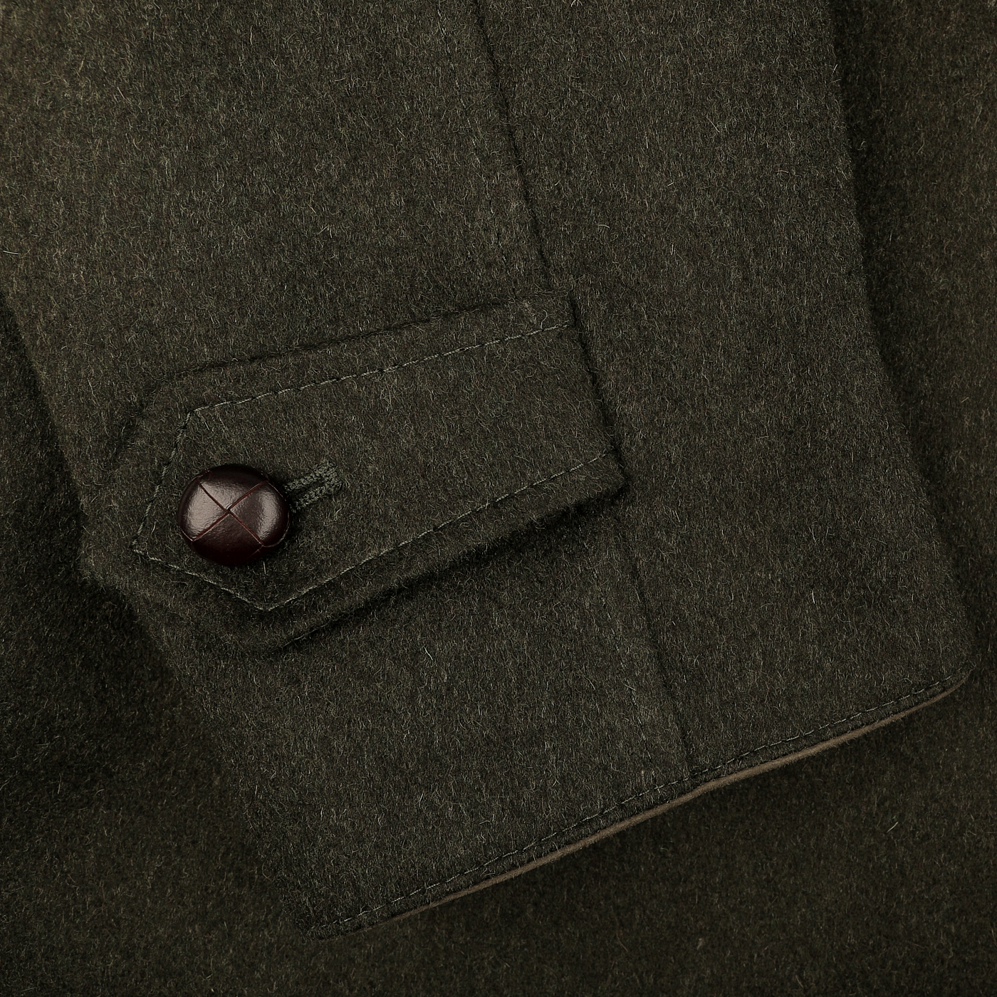 Close-up of the sleeve on Steinbock's Dark Green Wool Alpaca Loden Coat, showcasing a luxurious blend of wool and alpaca with a unique brown leather football button on the flap.