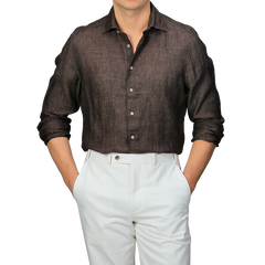 The person is showcasing a stylish Stenströms Dark Brown Linen Cutaway Slimline Shirt with sleeves rolled up, paired elegantly with white pants. This summer essential exudes a relaxed yet chic look, hands casually in pockets.