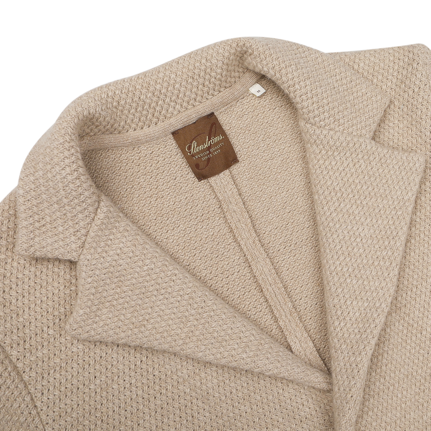 Close-up of the Beige Merino Wool Knitted Blazer from Stenströms, showcasing its textured design with a collar and tailored waist. It features an inside label that reads "Seawool," perfectly combining the elegance of a knitted blazer with the luxurious touch of merino wool.