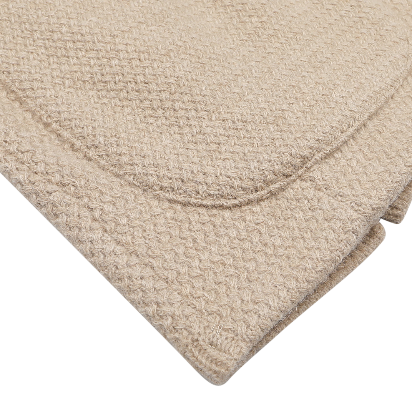 A close-up of a folded light beige textured blanket with a subtle woven pattern, echoing the intricate design of the Stenströms Beige Merino Wool Knitted Blazer, is placed on a white surface.